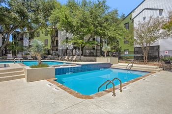 A small pool with a metal ladder is surrounded by a concrete patio and a fence.